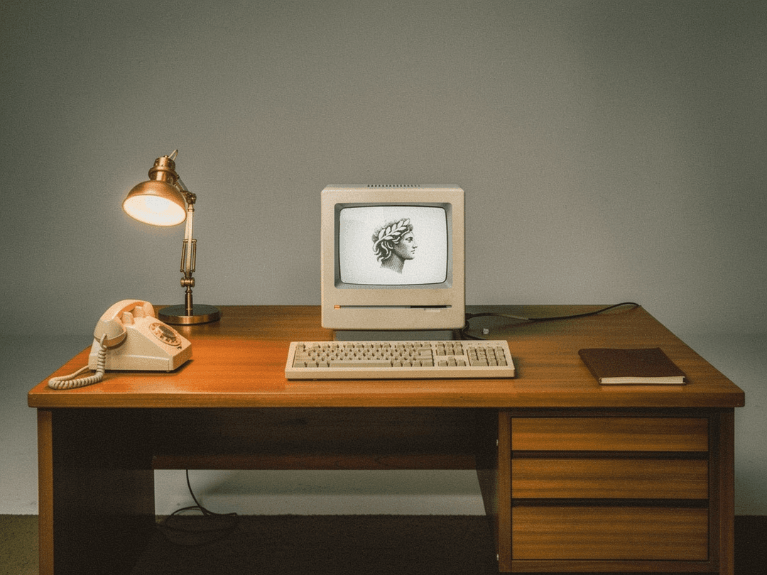 Retro desk with cream vintage computer, rotary phone, and brass lamp
